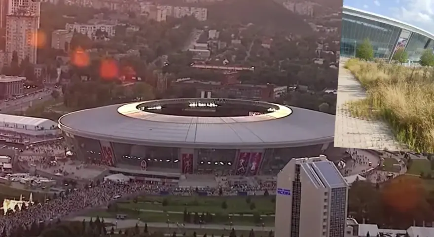 Donbass Arena w blasku zachodzącego słońca, otoczona miejskim krajobrazem i tłumami ludzi.