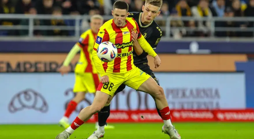 Piłkarz w żółto-czerwonej koszulce walczy o piłkę z rywalem w czarnym stroju. Intensywny przebieg: Pogoń Szczecin – Korona Kielce.