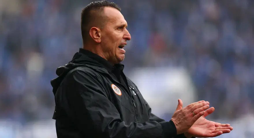 Trener Zagłębia Lubin, w czarnej kurtce, z otwartymi ustami i klaszczącymi dłońmi, motywuje drużynę.