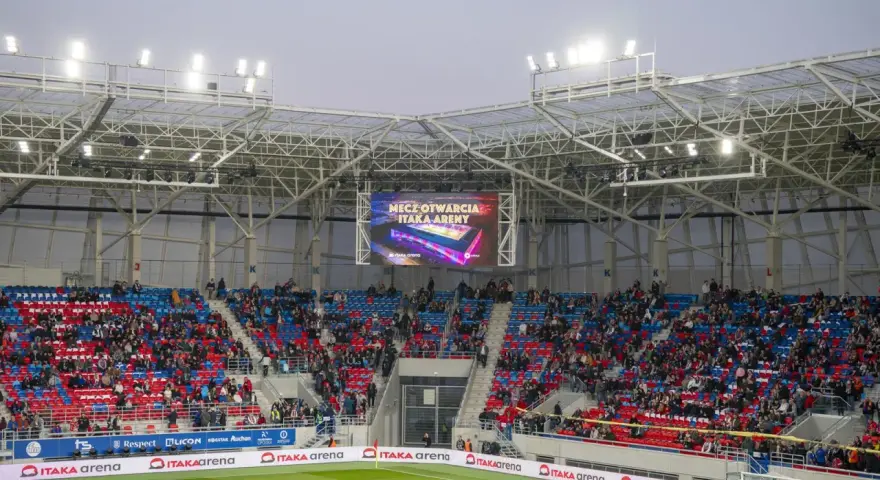 Widownia na stadionie Odra Opole podczas meczu otwarcia. Kolorowe trybuny i wielki ekran z napisem "Mecz otwarcia Itaka Areny".
