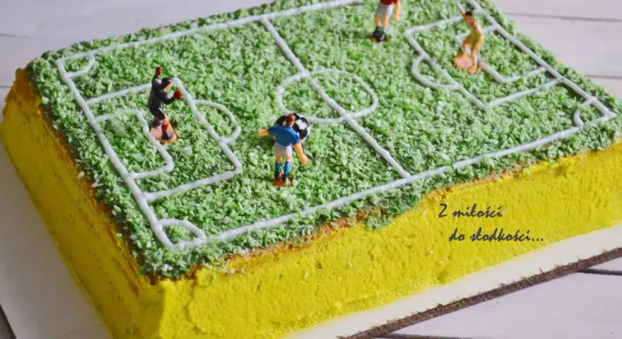 Jak zrobić tort boisko do piłki nożnej? Zielona posypka imituje trawę, a białe linie wyznaczają pole gry. Figurki piłkarzy i piłka dodają realizmu.