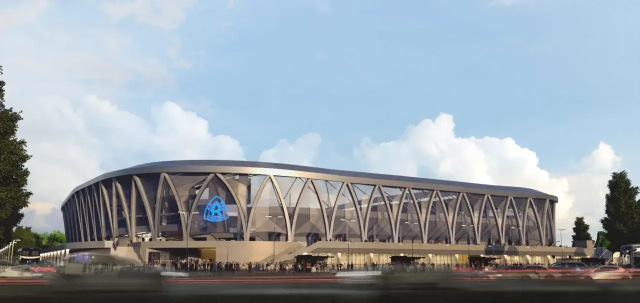 Nowy stadion Ruchu Chorzów z nowoczesną fasadą i charakterystycznym logo klubu. Tłumy kibiców i samochody tworzą dynamiczną scenę.