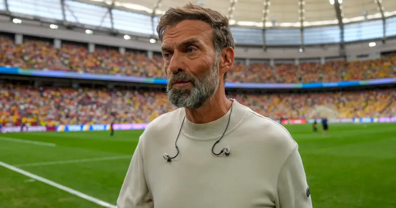 Trener reprezentacji Niemiec, z brodą i słuchawkami, na tle trybun stadionu.