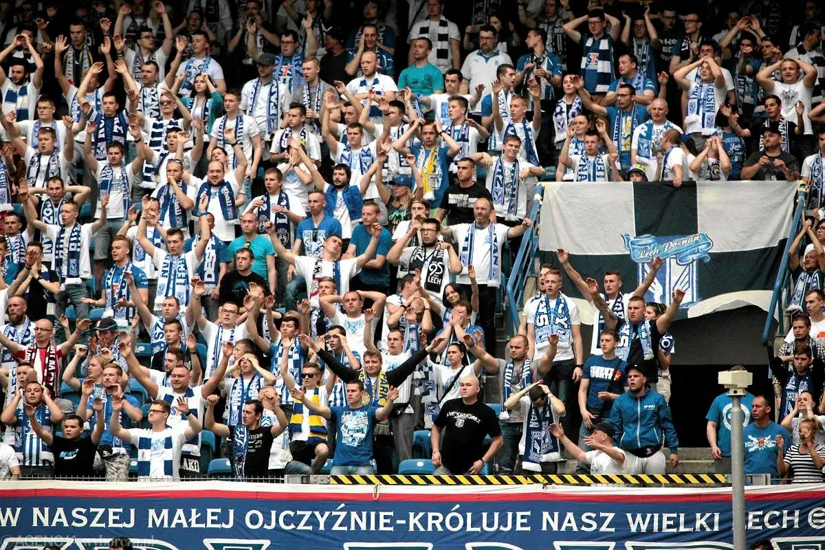 Tłum kibiców Lecha Poznań, wielu w szalikach, z flagą klubu. Sprawdź lech poznań bilety cennik, by dołączyć do tej atmosfery!