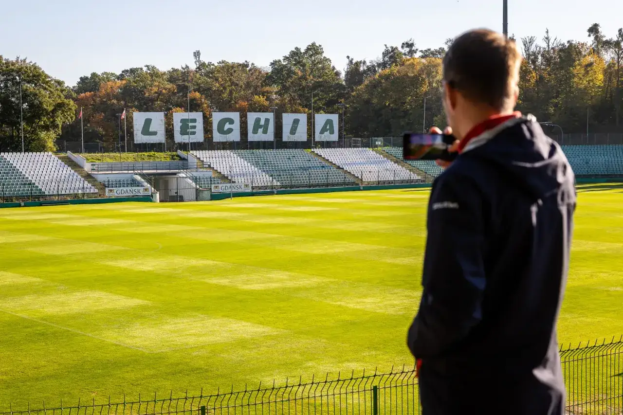 Widok na stadion Lechii Gdańsk. Mężczyzna z telefonem w ręku dokumentuje pusty stadion, czekając na powrót piłkarzy z Gdańska.