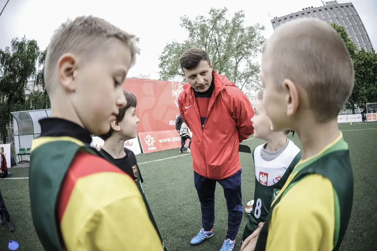 Trener w czerwonej kurtce tłumaczy młodym piłkarzom, jak zostać piłkarzem w wieku 13 lat.