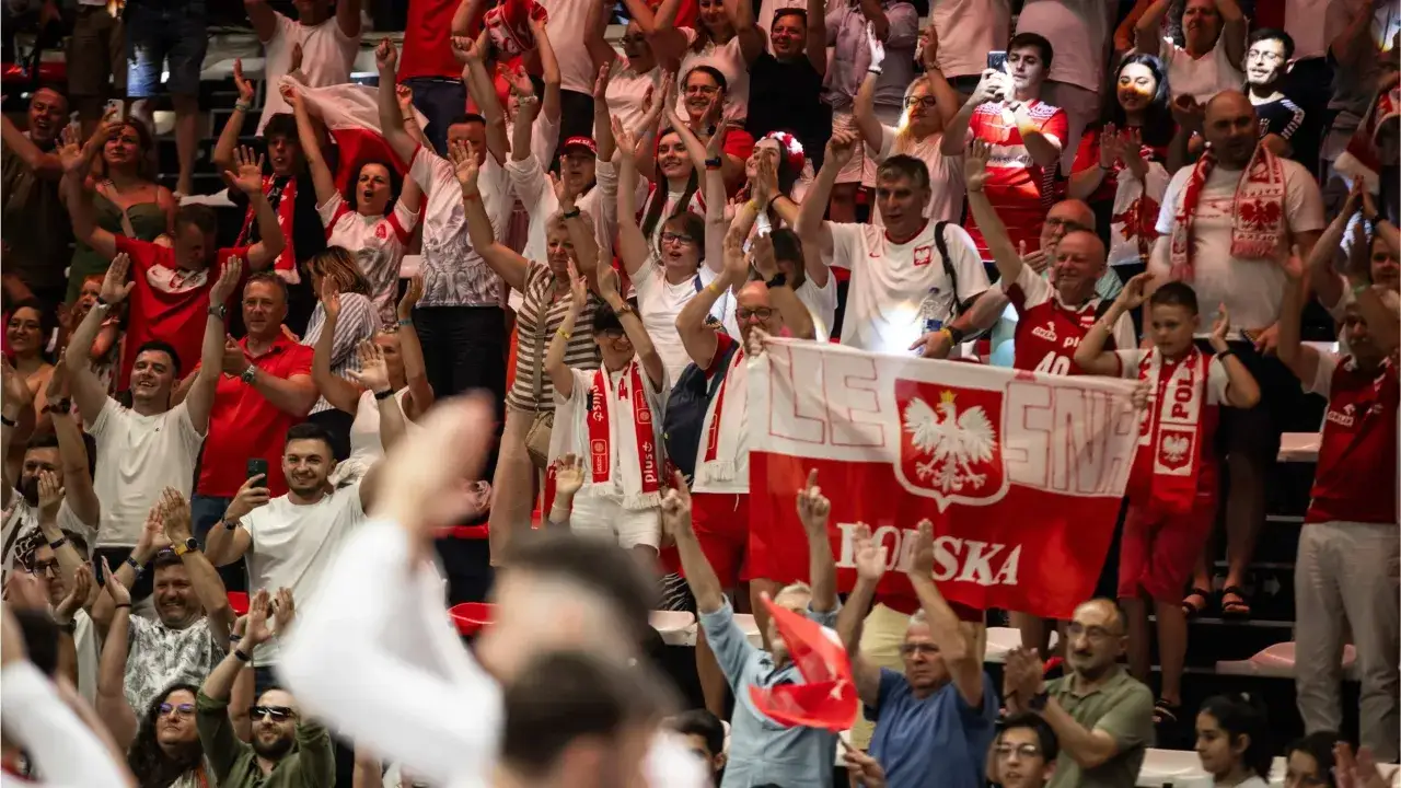 Tłum kibiców z flagami Polski, zastanawiający się, ile kosztuje bilet na mecz siatkówki reprezentacji Polski.