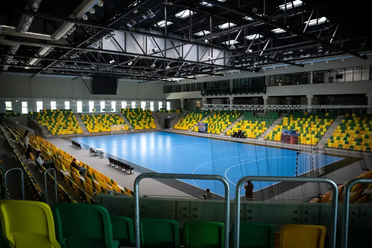 Pusta hala sportowa z niebieską podłogą i żółto-zielonymi trybunami. Czekamy, kiedy mistrzostwa w piłce ręcznej rozpoczną się na tym boisku.