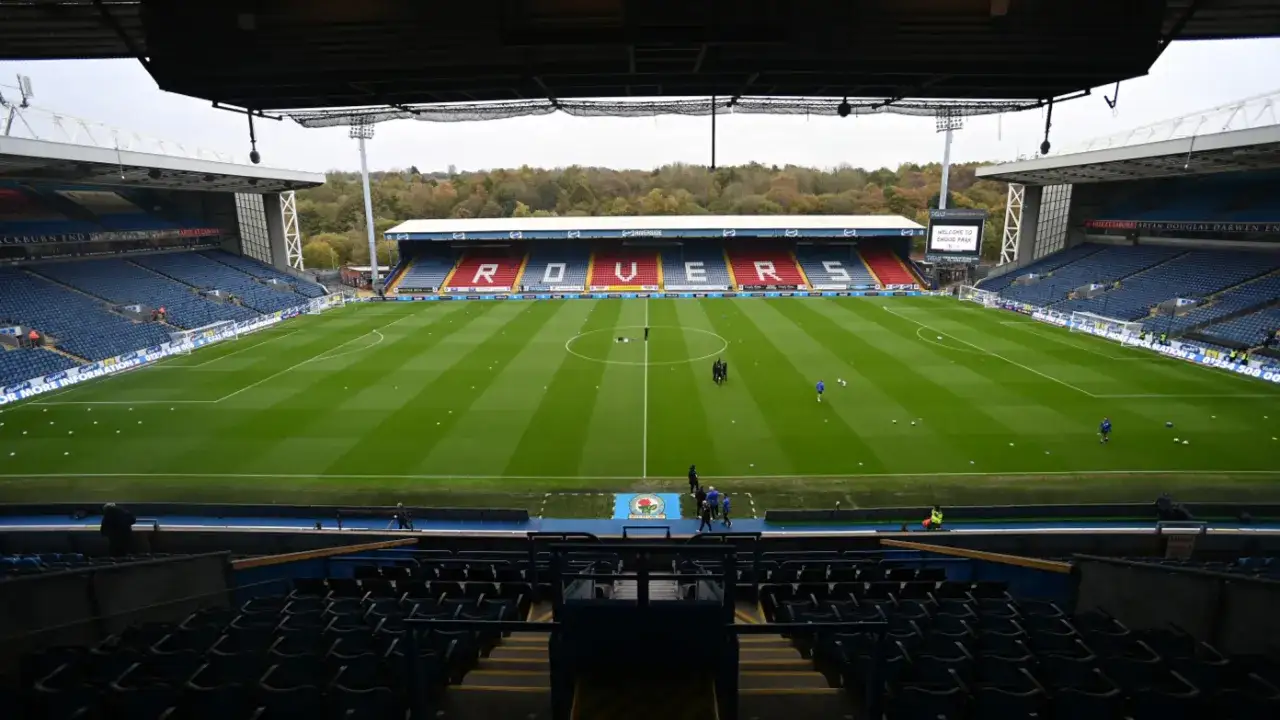 Puste trybuny stadionu Ewood Park, z zieloną murawą i napisem 