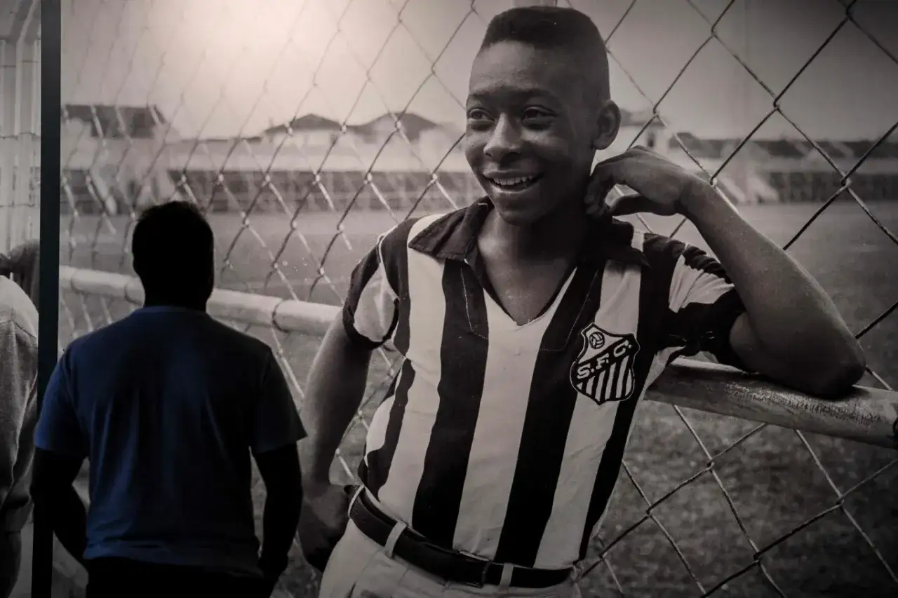 Młody Pelé w koszulce Santos FC, uśmiechnięty, oparty o siatkę. Jego niesamowite pelé statystyki zaczynały się właśnie wtedy.