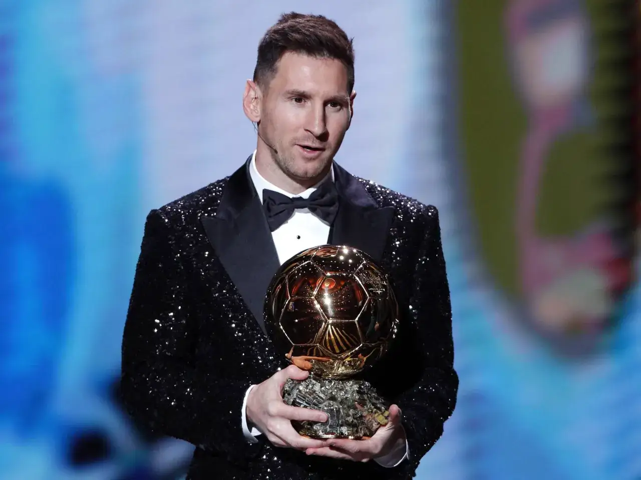 Lionel Messi w błyszczącej marynarce trzyma Złotą Piłkę.