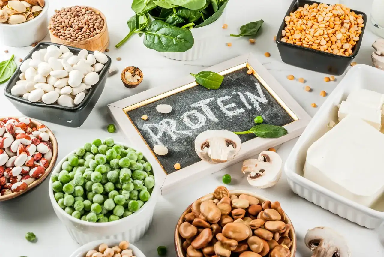 Biała tabliczka z napisem PROTEIN otoczona fasolą, grochem, soczewicą, szpinakiem i tofu. Czy można brać białko bez treningu? Tak, dla zdrowia!