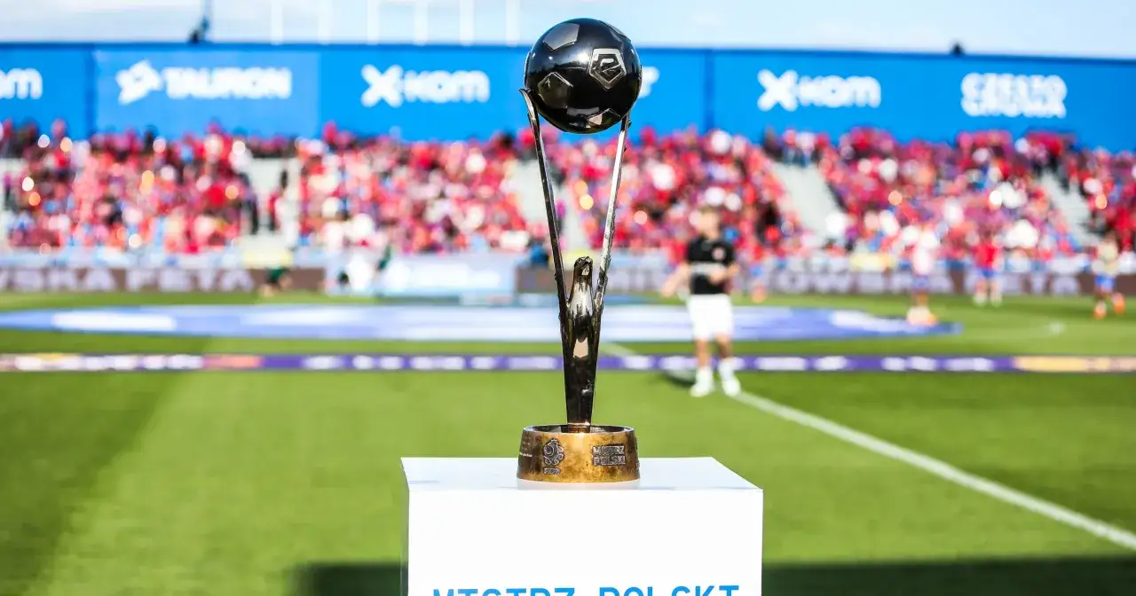 Trofeum czeka na tego, kto mistrzem ekstraklasy zostanie. Piłkarski puchar na tle trybun pełnych kibiców.