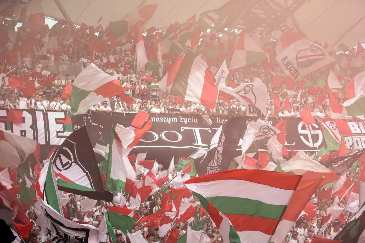 Tłum kibiców z flagami w barwach Legii Warszawa, atmosfera ostatniej kolejki Ekstraklasy.