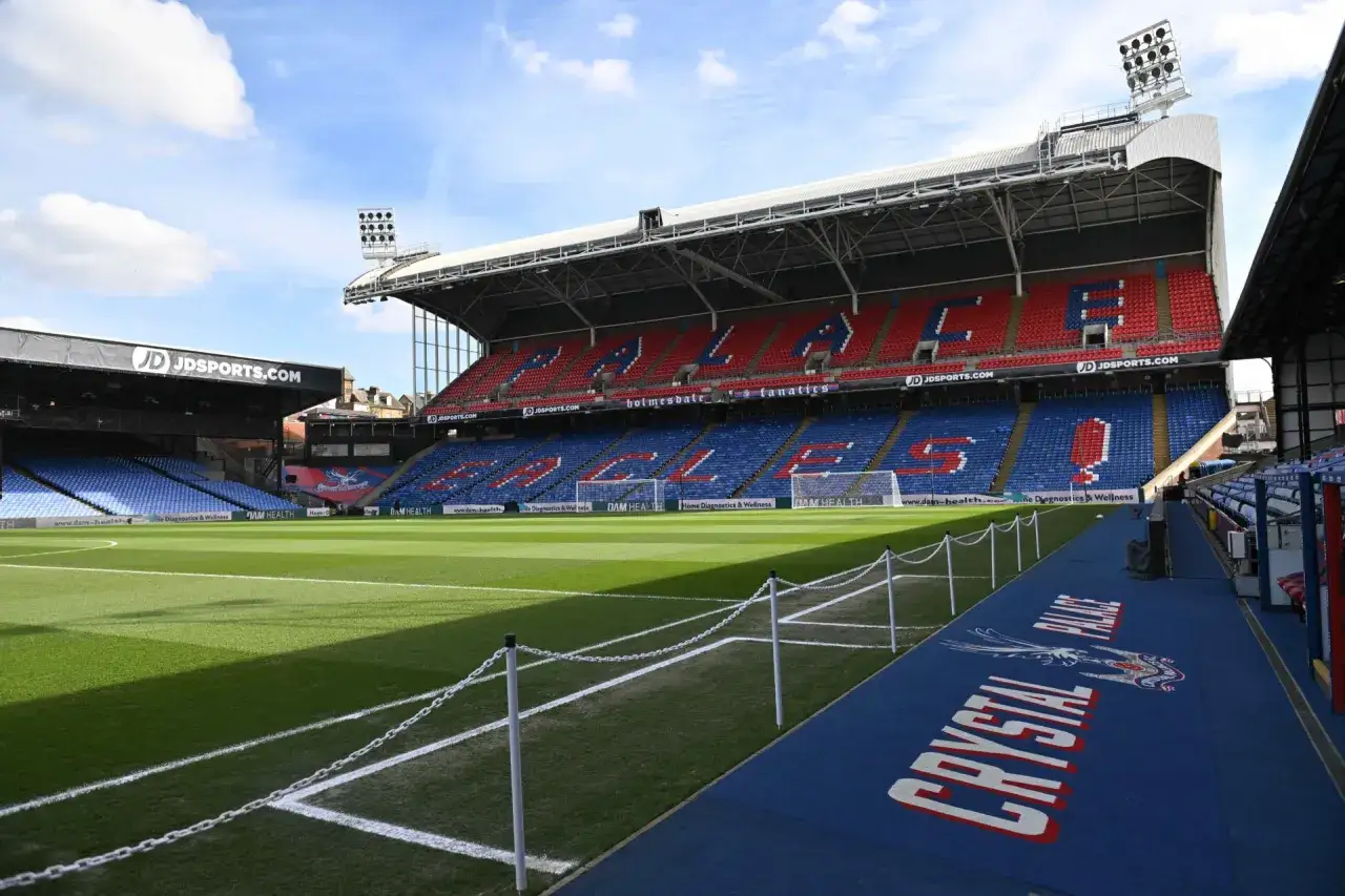 Puste trybuny stadionu Selhurst Park, z czerwonymi i niebieskimi siedzeniami tworzącymi napisy.
