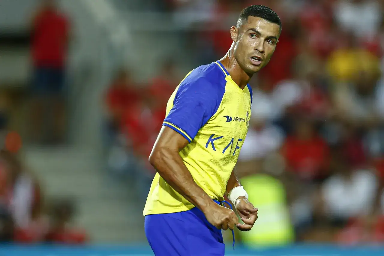 Piłkarz Cristiano Ronaldo w żółtej koszulce z niebieskimi rękawami, skupiony na boisku. Jego zarobki tygodniowe piłkarzy budzą podziw.