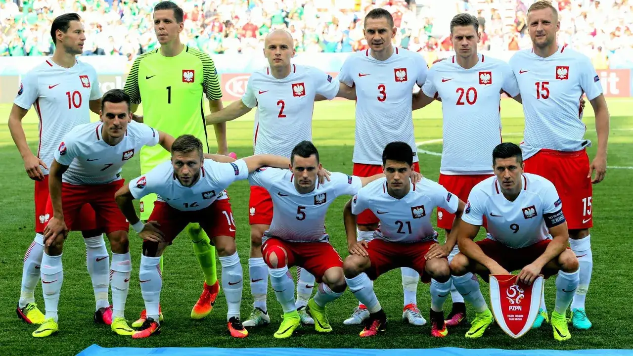 Drużyna Polski w piłce nożnej, gotowa do gry. Widać jedenastu zawodników w białych koszulkach i czerwonych spodenkach.