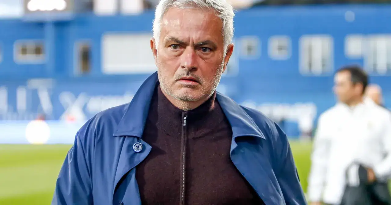 Jose Mourinho, były trener Realu Madryt, w granatowej kurtce i brązowym golfie, zamyślony na tle stadionu.
