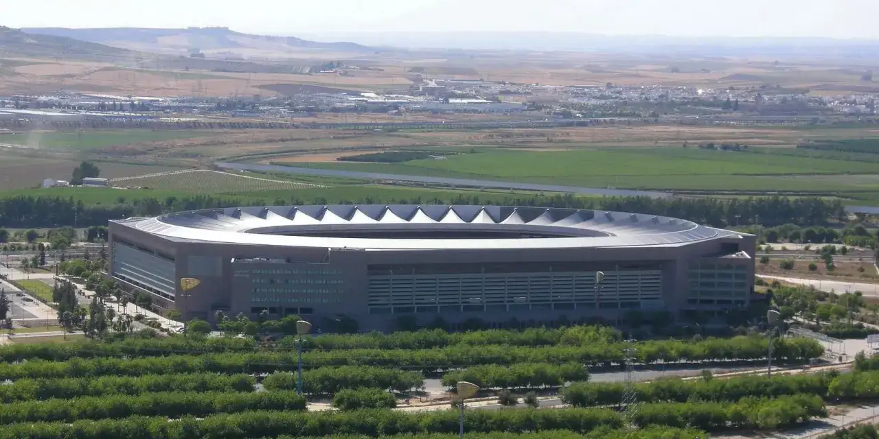 Stadion La Cartuja w Sewilli, otoczony zielenią i polami, góruje nad krajobrazem.