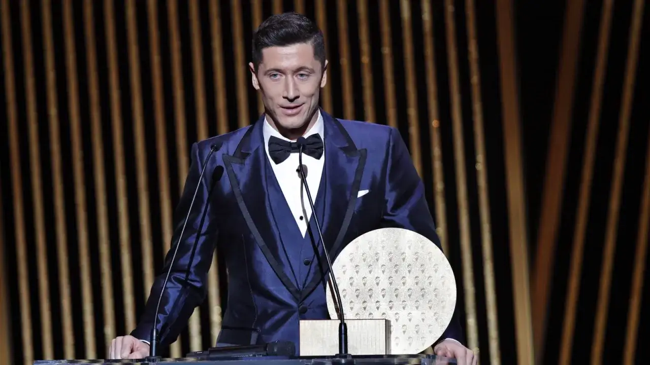Robert Lewandowski w garniturze stoi przy mównicy z Złotą Piłką.