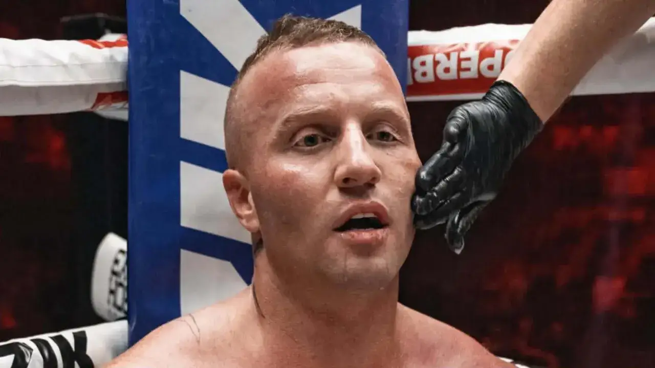 Denis Załęcki, znany z walk freak fight, w ringu. Jego twarz jest spocona, a ręka w czarnej rękawiczce dotyka jego policzka.