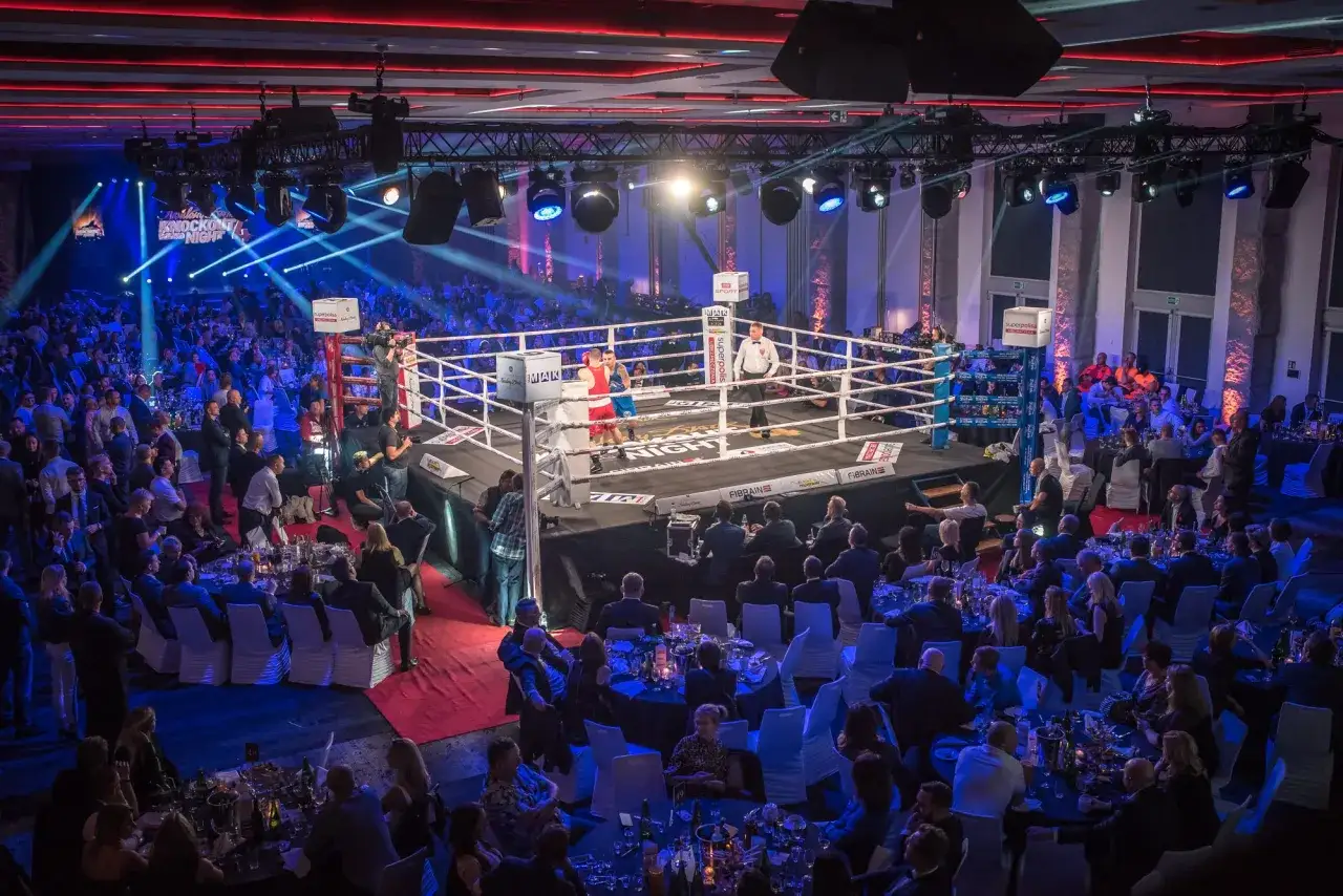 Widownia w eleganckich strojach obserwuje zmagania bokserów podczas rocky boxing night.