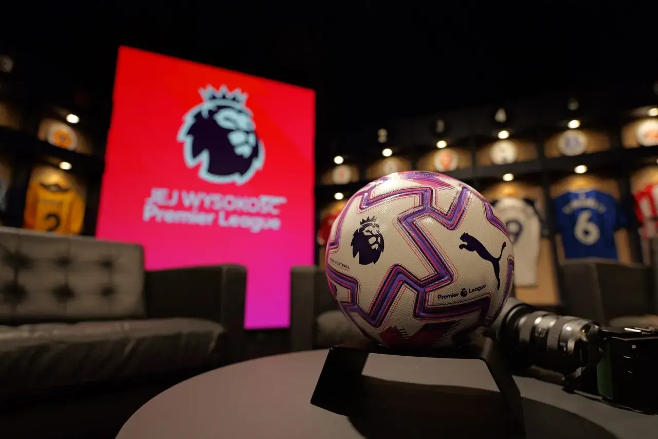 Piłka Premier League na stoliku, w tle ekran z logo ligi i kanapy. Idealny pakiet Canal Plus Sport dla fanów piłki nożnej.