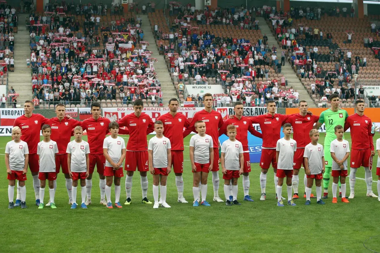 Dzieci w strojach piłkarskich stoją obok piłkarzy reprezentacji Polski. Dowiedz się, jak zgłosić dziecko do wyprowadzania piłkarzy.