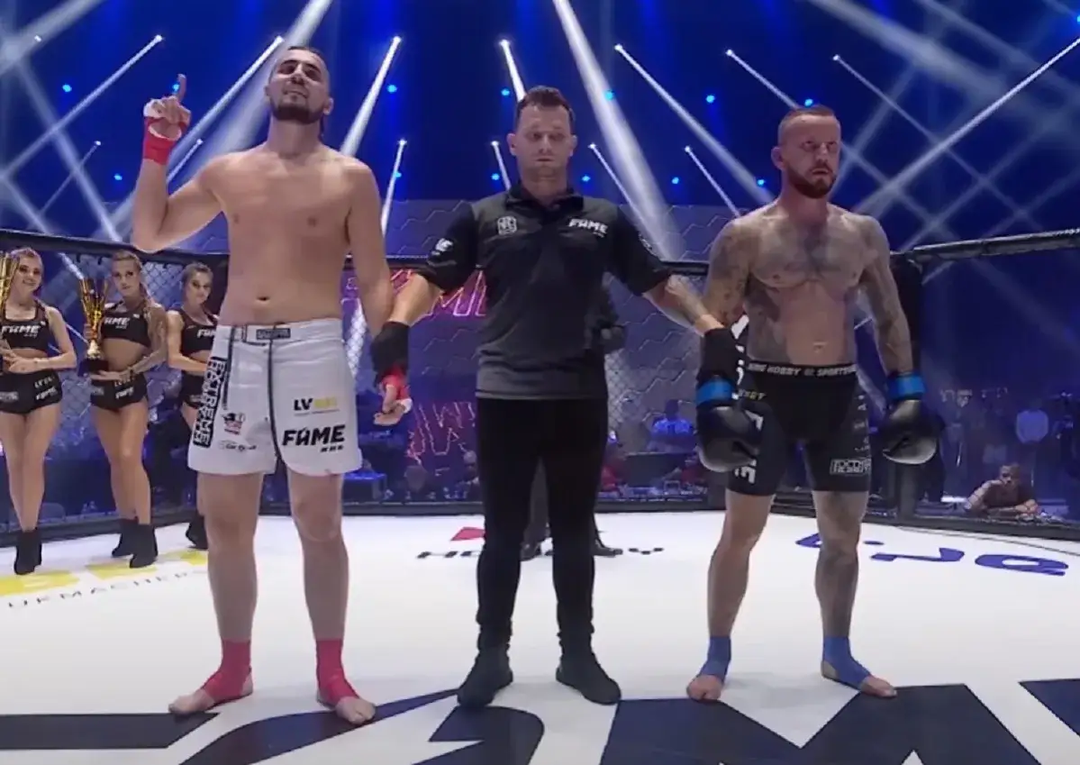 Sędzia ogłasza zwycięzcę gali FAME MMA. Dwóch zawodników, ring girls z pucharem.